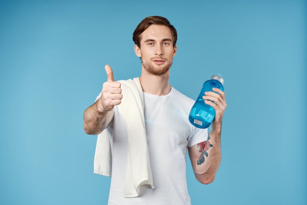 Sporty man showing thumb up water bottle towel on shoulder cropped view blue background