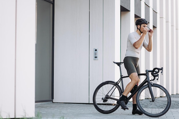 Sporty man sitting on black bike and putting on mirrored glasses and safety helmet outdoors Caucasian athlete preparing for morning cycling on city streets