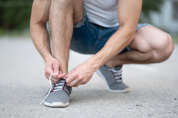 A sporty man ties the laces on his sneakers before running on the street close up