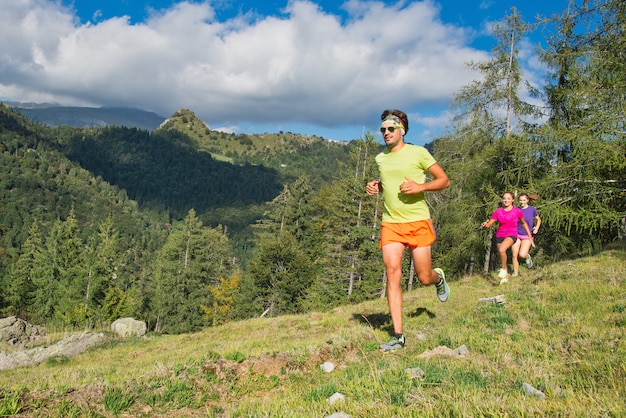 Sporty man and young girls running together on the grass in a mo