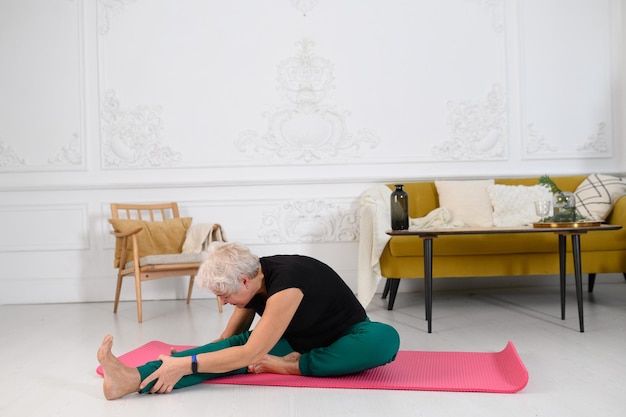 Sporty senior woman doing yoga while watching tutorial on laptop