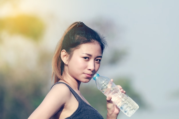 Sporty woman asia holding and drinking water outdoor on sunny day