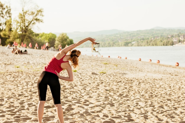 Photo sporty woman doing body stretching at the beach, back view.