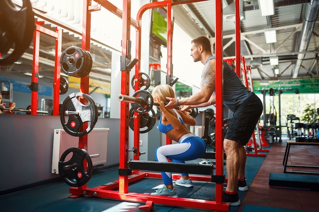 Sporty woman doing weight exercises with assistance of her personal trainer at gym