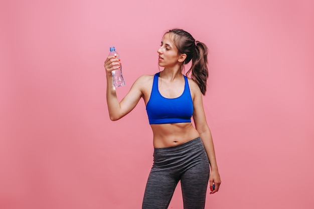 Sporty woman drinking water on pink wall