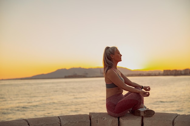 Sporty woman meditating in lotus position on embankment