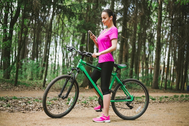 Sporty Woman on Mountait Bicycle in Forest while riding with Phone in Hand Apps for Bike Sport