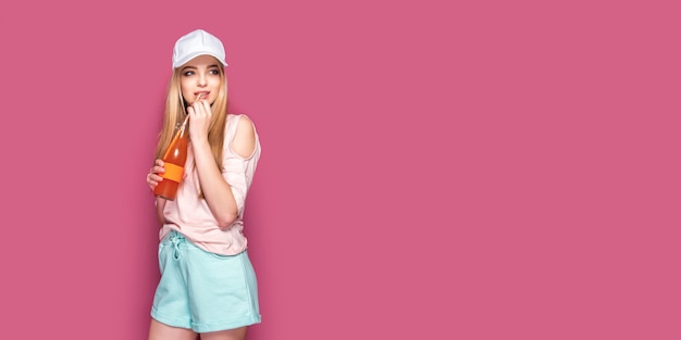 Sporty woman with cold drink standing on pink wall