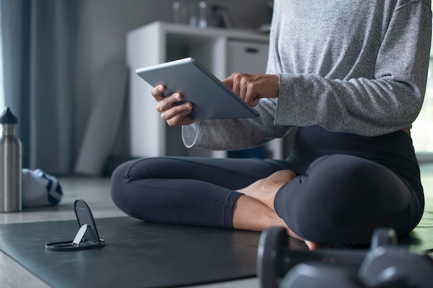 Sporty young Asian woman exercising at home watching fitness video on Internet or having online fitness class using tablet living room interior copy space