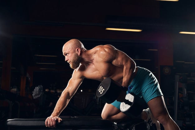 Sporty young man lifting weights while doing a physical exercise in a gym