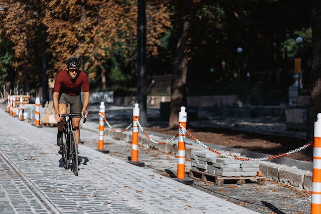 Sporty young man in safety helmet and mirrored glasses riding bike on empty road during repairing. Caucasian cyclist training outdoors during free time.