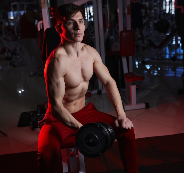 Sporty young man training with dumbbells against dark background