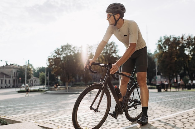 Sporty young man wearing active clothes helmet and glasses sitting on black bike outdoors Relaxation after workout Lifestyles concept