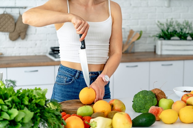 Sporty young woman is cutting fresh orange for fruit juice in the kitchen