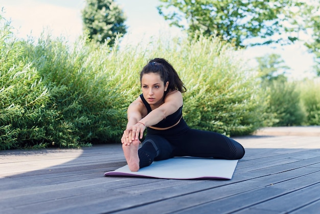 Sporty young woman makes yoga exercising with yoga mat at the park outdoor active lifestyle concept