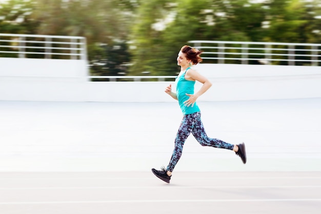 Sporty young woman running by allseason track at the city stadium