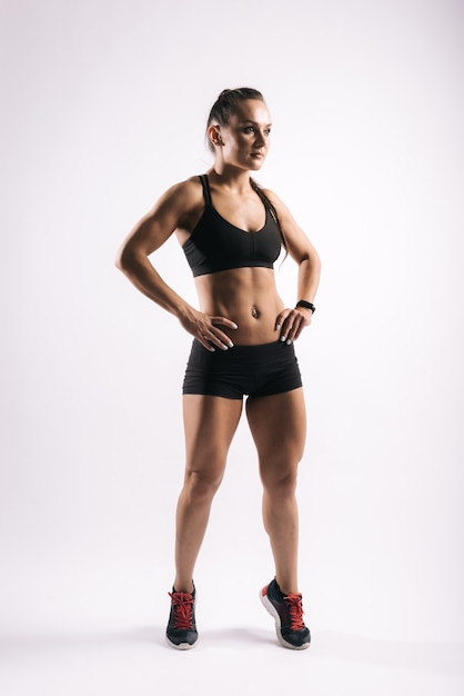 Sporty young woman with perfect muscular body is standing with hands on her belt