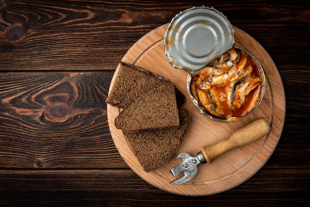 Sprats in tomato sauce on dark wooden table.