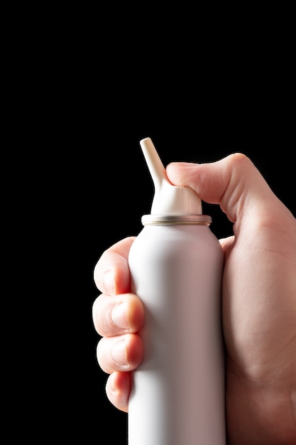 Spray bottle with salt sea water for nasal cavity hygiene in female hand isolated on black background