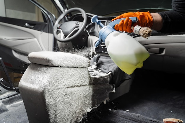 Spraying detergent on dashboard in car interior for dry cleaning Professional cleaner in gloves is pouring detergent in car for removing stains and dirt