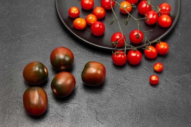 Sprig of cherry tomato on black plate Red tomatoes on the table