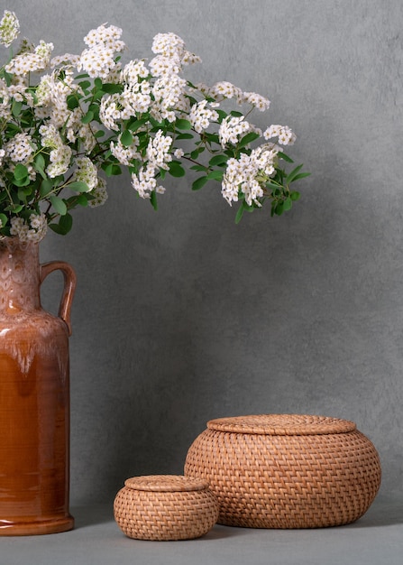 Sprigs of white flowers in a brown vase on a gray background next to two round baskets