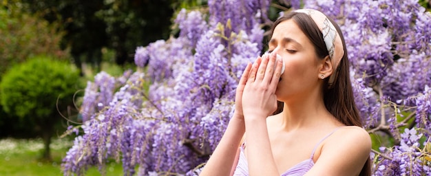 Spring allergy flu banner sick woman sneezing covering nose with a wipe in a park spring allergy con