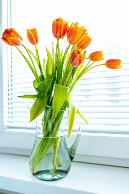 Spring bright yellow orange tulips in glass jar on windowsill close-up