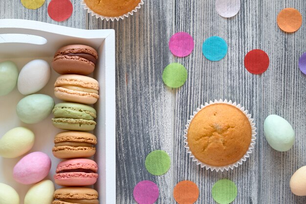 Spring celebration flat lay with macarons, muffins and marzipan eggs jn a decorative tray on grey wood