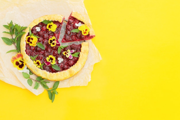 Spring cherry pie, decorated with edible flowers on a yellow. 