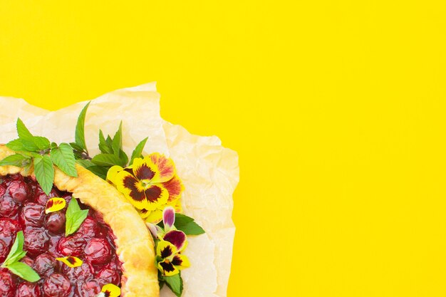 Spring cherry pie, decorated with edible flowers on a yellow. 