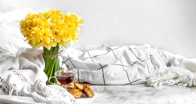 Spring composition with a bouquet of daffodils and tea with cupcakes on a cozy light table.