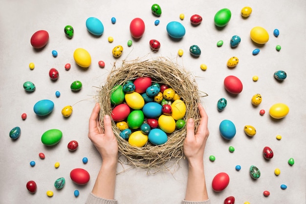 Spring Easter background Female hands hold a nest with Easter colorful eggs Easter flat lay decoration Holiday in spring season Top view abstract creative composition Spring mood