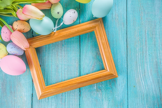 Spring and Easter holiday background with tulip flowers, colorful pastel eggs on blue table top view. Happy Easter greeting card.