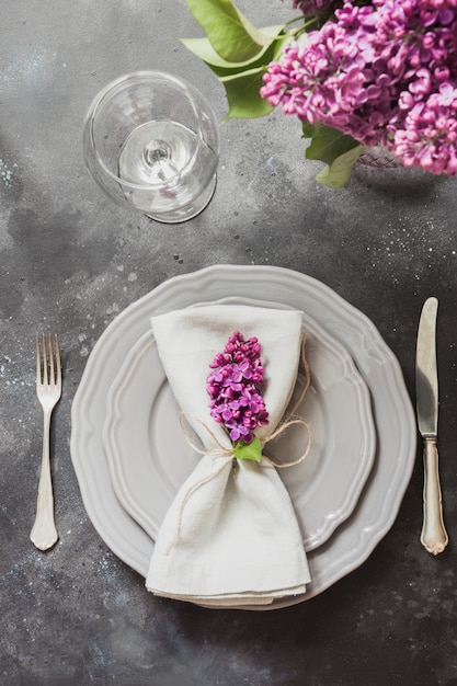 Spring elegant table place setting with violet lilac, silverware on vintage table. 