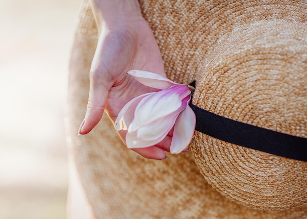 Spring flowering Open aperture with light blurring and illumination A womans hand with a flower on the background of a straw hat with a large brim Spring