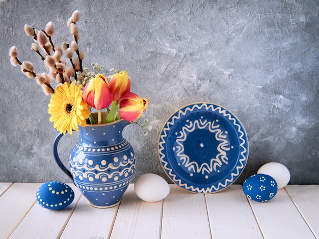 Spring flowers in blue ceramic pitcher with matching plate and  Easter eggs on gray