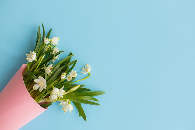 Spring flowers bouquet in pink paper cone on blue background flat lay Happy Mothers day