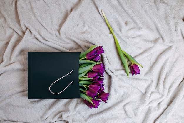 Spring flowers, bunch of purple tulips in black paper bag on the beige plaid.