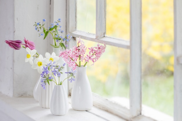 Spring flowers in white vase on old windowsill