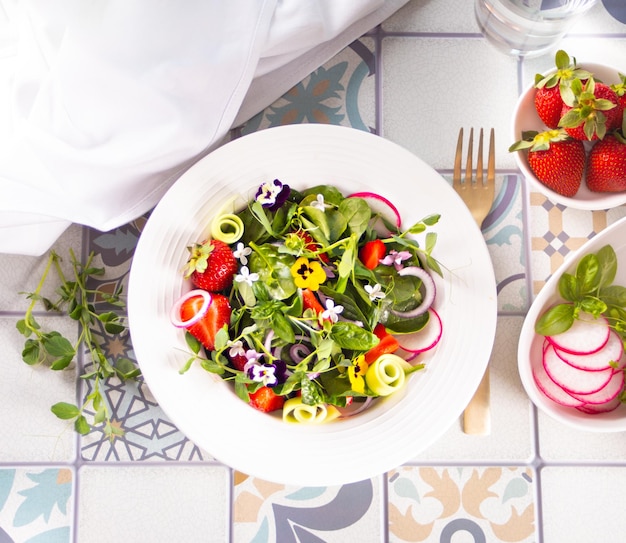 Spring healthy fresh salad with green edible flowers pansies viola and strawberries