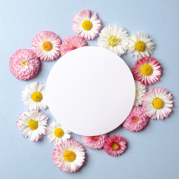 Spring holiday concept. Creative layout made of colorful flowers and blank circle-shaped paper card on pastel blue background. 