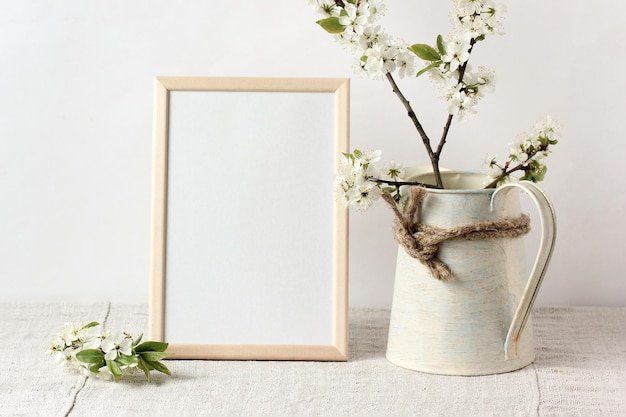 Spring mockup with an empty frame on the table and flowering branches in a jug