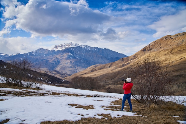 Spring in the mountains, the snow melted. The girl photographer shoots the landscape.