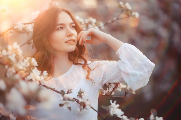 spring portrait of an adult happy woman in a blooming garden, sun rays and glare, april flowers girl