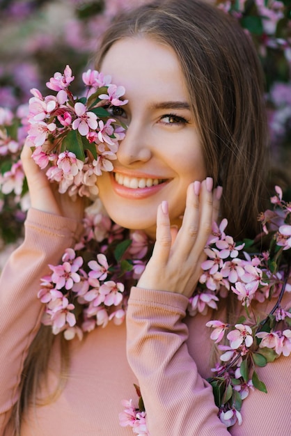 Spring portrait of a beautiful smiling happy girl under a blooming apple tree with pink flowers