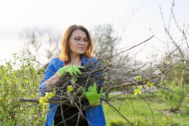 Spring pruning of trees and bushes in the garden Woman gardener in gloves with dry branches of bushes and fruit trees Hobby gardening farm concept