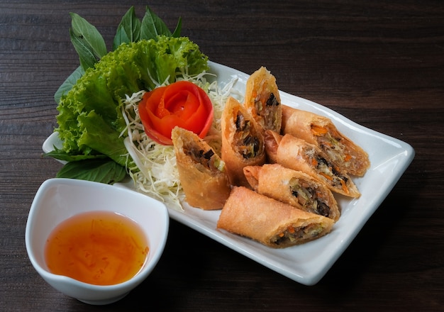 Spring rolls on white dish with dark wooden table background.