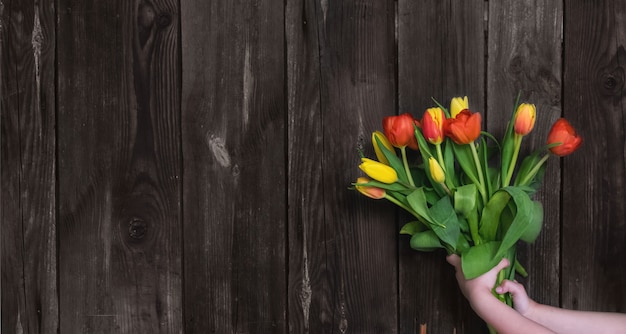 Spring sale A bouquet of fresh red and yellow tulips in the girl s hand on wooden background