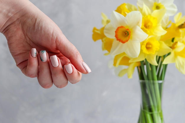 Spring or summer neat nude manicure with floral ornament against blurred flowers Fashion and beauty